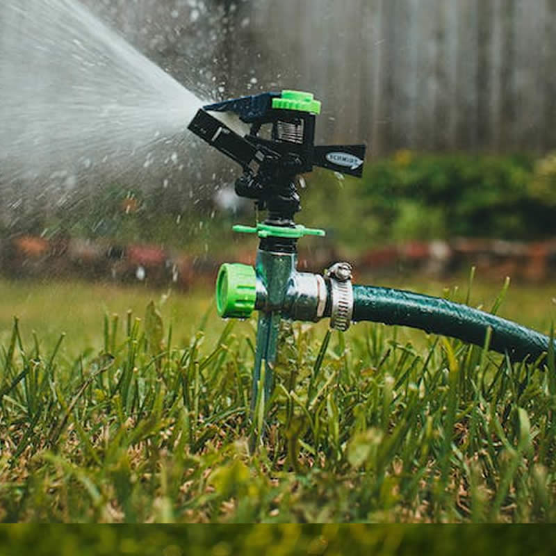 A sprinkler set in grass, spritzing water over lawn